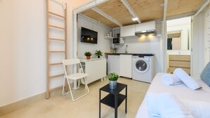 Habitació petita amb llit, taula amb una planta, cadira, rentadora, microones i televisió.