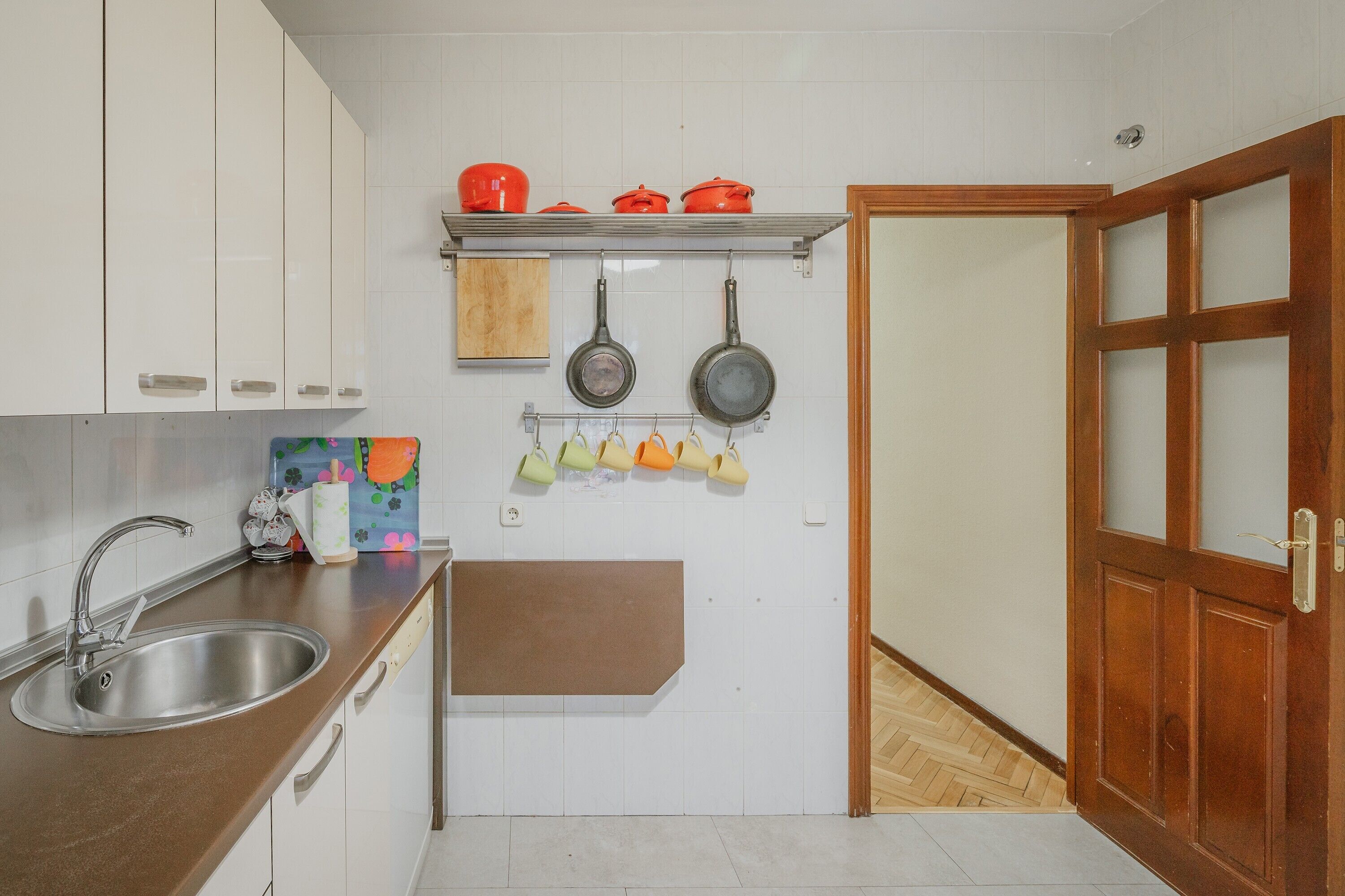 A kitchen with a sink, cabinets, a shelf with pots, pans, and hanging cups.