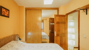 A bedroom with a bed, a wooden wardrobe, a mirror, and a bedside lamp.