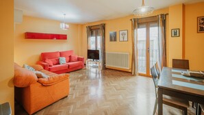 A living room with a red sofa, a television, and a dining area with a table and chairs.