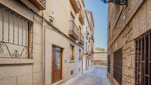 A narrow cobblestone street flanked by historic buildings with barred windows and balconies.