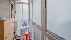 A narrow balcony with a white chair, a red stool, and a wooden cabinet.