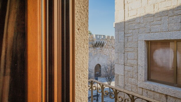 A stone building with a balcony, a wrought iron railing, and a window with blinds.
