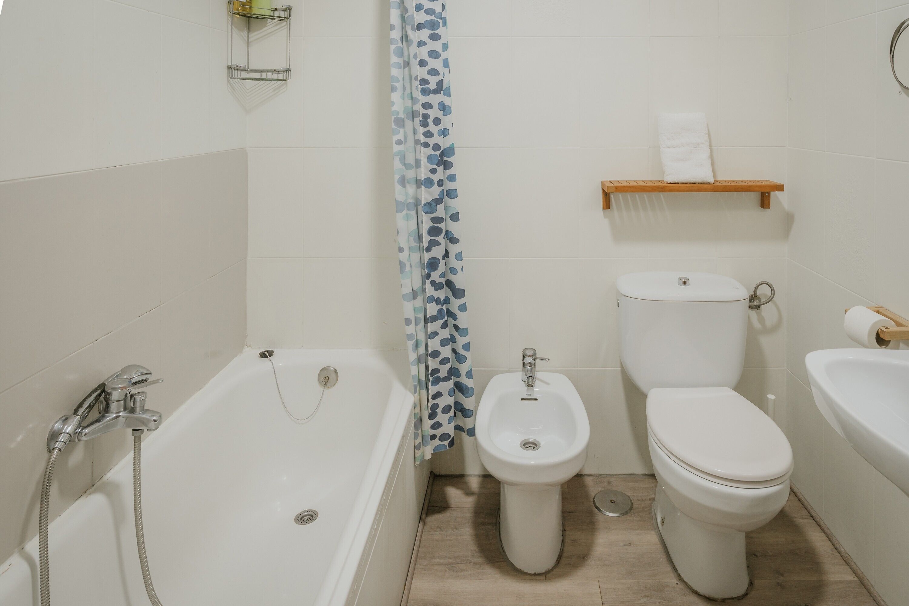 Un baño con bañera, bidé, inodoro y un estante con una toalla.