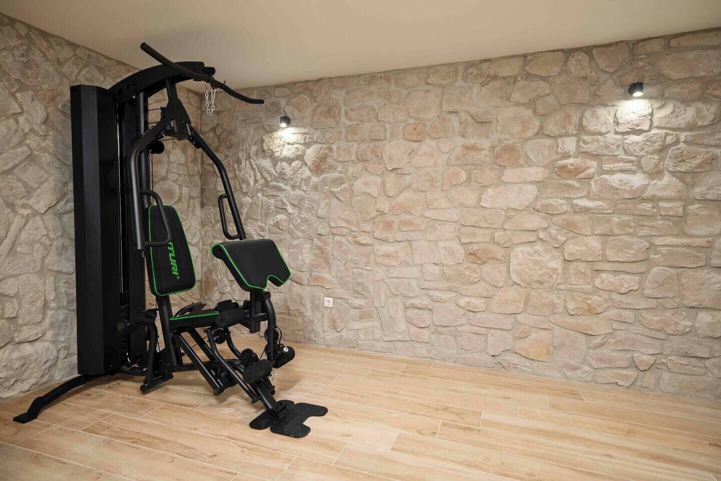 A room with a stone wall and a wooden floor, featuring a black exercise machine with green accents.