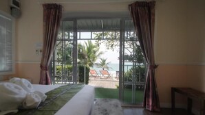 A hotel room with a bed, a view of the beach, and a balcony with chairs. - Pattaya Paradise Beach Resort (Sattahip)