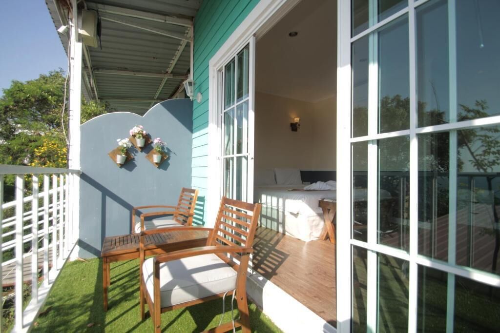 Un balcon avec deux chaises en bois et une petite table, une clôture blanche et une fenêtre donnant sur l’extérieur.