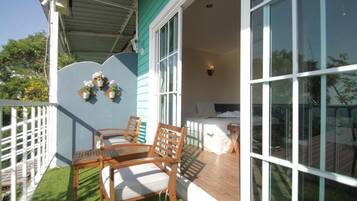 Un balcon avec deux chaises en bois et une petite table, une clôture blanche et une fenêtre donnant sur l’extérieur.