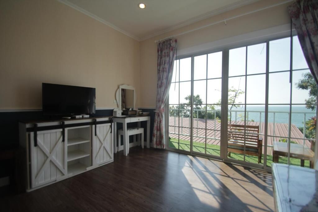 Ein Zimmer mit Fernseher, einem kleinen Tisch und einem großen Fenster mit Meerblick.