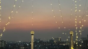 Eine Stadtansicht im Abenddämmerung mit Lichterketten und zwei markanten Lichtmasten.