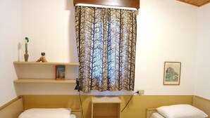 A small, cozy bedroom with two single beds, a shelf with books and a vase, and a curtain with a tree pattern. - Nice Villa With a Fenced Garden (San Michele al Tagliamento)