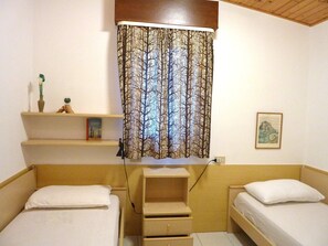 A small, cozy bedroom with two single beds, a shelf with books and a vase, and a curtain with a tree pattern. - Nice Villa With a Fenced Garden (San Michele al Tagliamento)