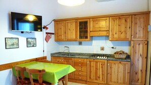 A kitchen with wooden cabinets, a gas stove, a sink, and a dining table with chairs. - Nice Villa With a Fenced Garden (San Michele al Tagliamento)