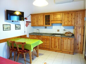 A kitchen with wooden cabinets, a gas stove, a sink, and a dining table with chairs. - Nice Villa With a Fenced Garden (San Michele al Tagliamento)