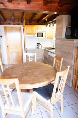 A wooden dining table with chairs, a kitchen area with a microwave and stove, and a wooden ceiling.
