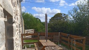 A wooden deck with a table and chairs, surrounded by a stone wall. - TY LOUTI Cottage – Gateway to Huelgoat and Monts d’Arrée (Plouyé)