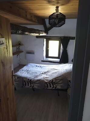Une chambre avec un lit, une fenêtre, un luminaire suspendu et des poutres en bois.