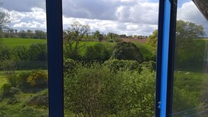 A view through a window with a clear sky, green fields, and trees. - TY LOUTI Cottage – Gateway to Huelgoat and Monts d’Arrée (Plouyé)