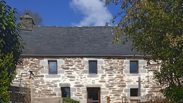 A stone building with a wooden door, a small window, and a paved area with a wooden bench. - TY LOUTI Cottage – Gateway to Huelgoat and Monts d’Arrée (Plouyé)