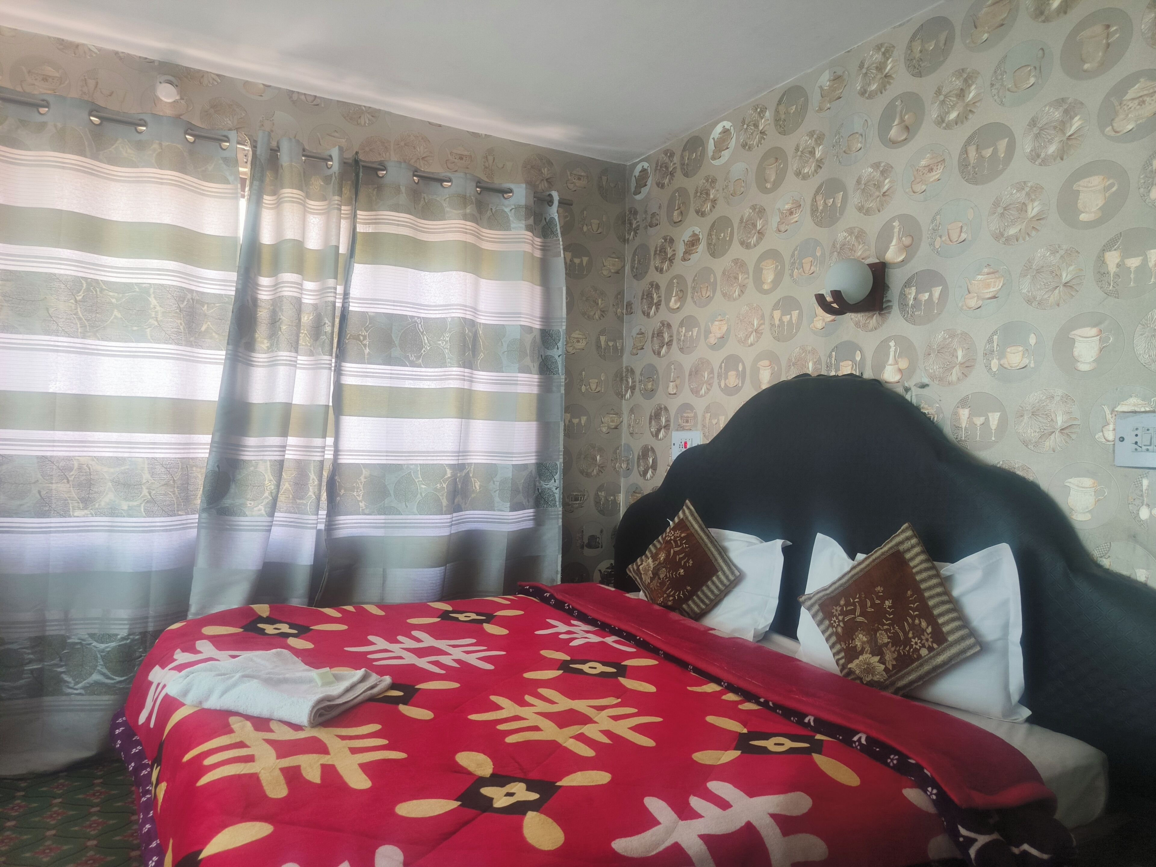 A room with a bed, curtains, patterned wallpaper, and a wall-mounted light.