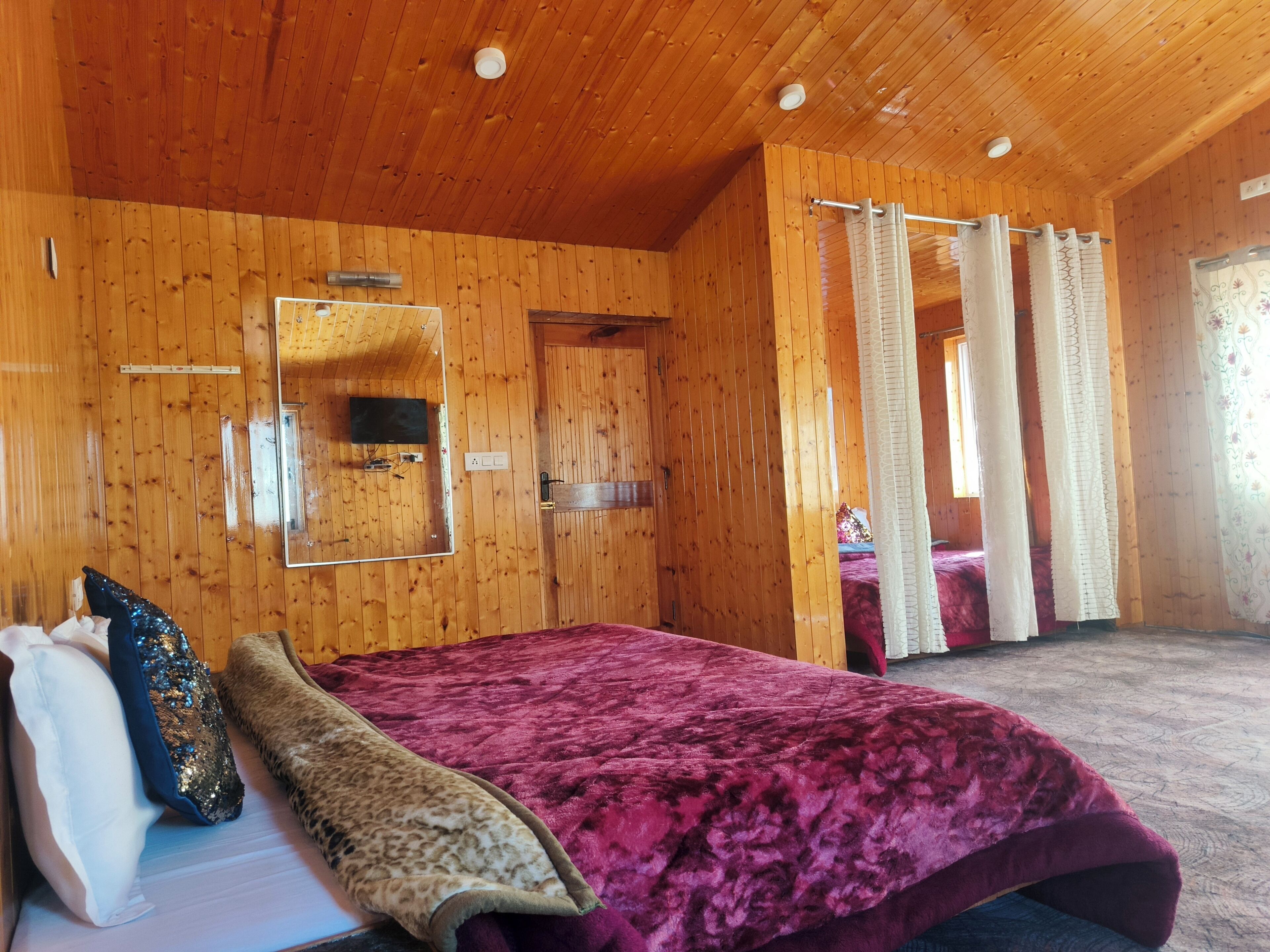 A wooden-paneled room with a bed, a mirror, and a television.