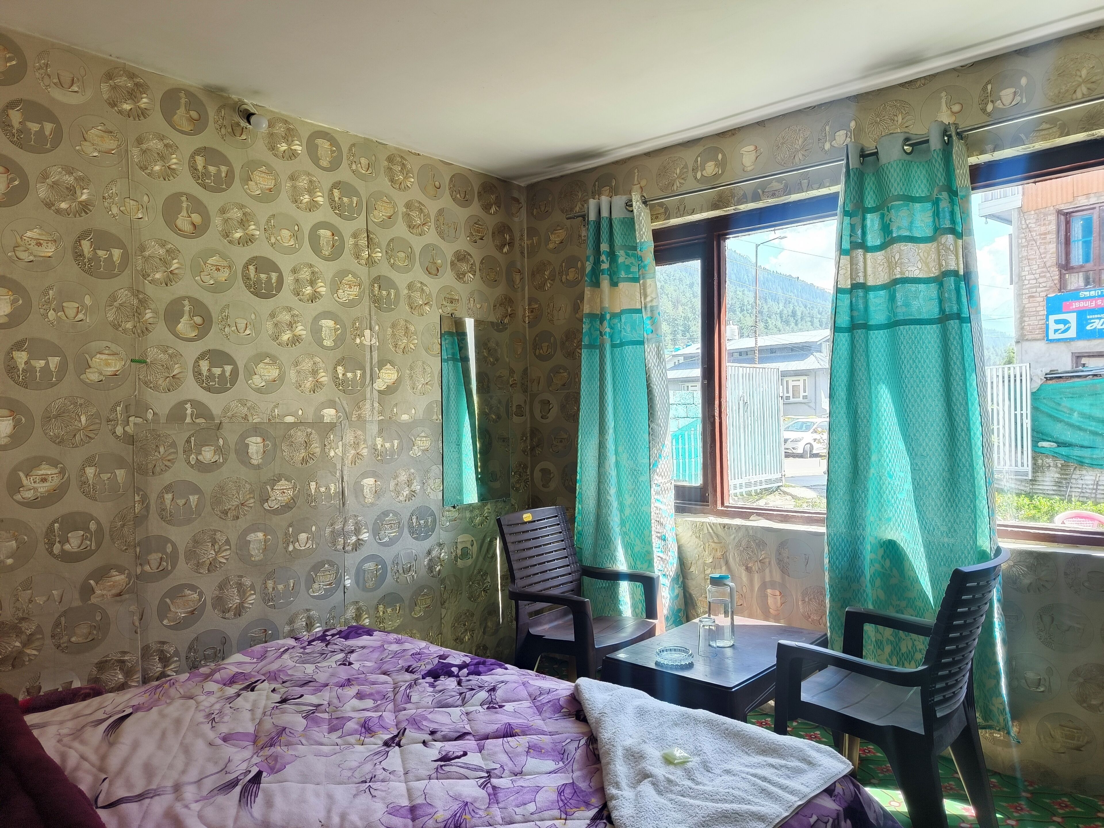 Una habitación con una cama, dos sillas, una mesa y un ventanal con cortinas.