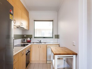 Une cuisine compacte avec des meubles en bois, un four encastré, un évier et une fenêtre située au-dessus du plan de travail.