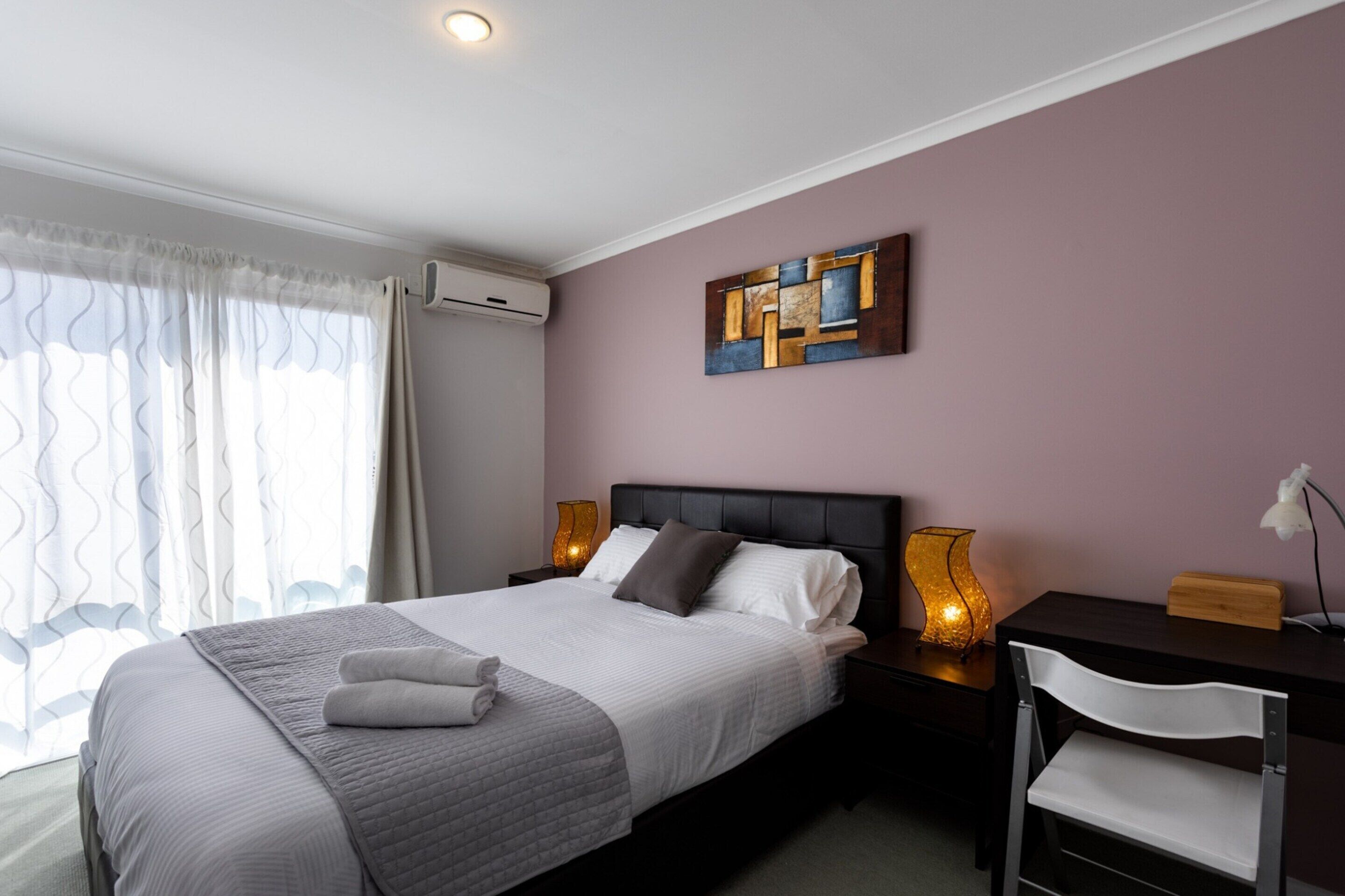 Un dormitorio ordenado con cama, lámparas de noche, escritorio y silla.