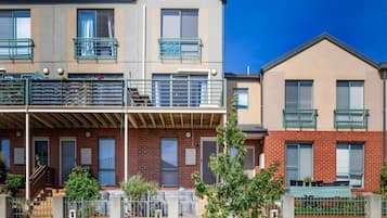 Una hilera de edificios residenciales de dos pisos con balcones, fachadas de ladrillo y un cielo azul despejado.