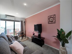 Un salon avec un canapé, un téléviseur, une table à manger avec des chaises et une plante en pot.