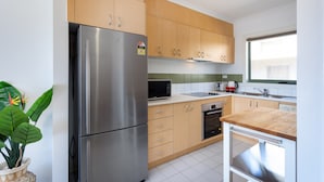 A modern kitchen with stainless steel appliances, wooden cabinets, and a window providing natural light. - Snug 2-bed Townhouse Near Bustling Shops (Melbourne)