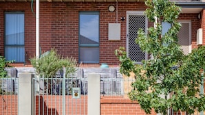 A two-story residential building with a balcony on the upper floor, a brick facade, and a metal gate in the foreground. - Snug 2-bed Townhouse Near Bustling Shops (Melbourne)