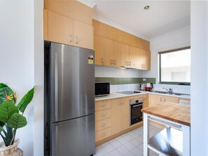 Une cuisine moderne dotée d’appareils électroménagers en acier inoxydable, de meubles en bois et d’une fenêtre laissant entrer la lumière naturelle.