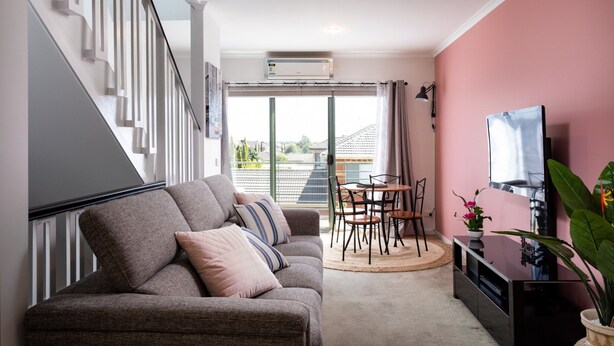 A modern living room with a grey sofa, a TV, a dining table with chairs, and a staircase. - Snug 2-bed Townhouse Near Bustling Shops (Melbourne)