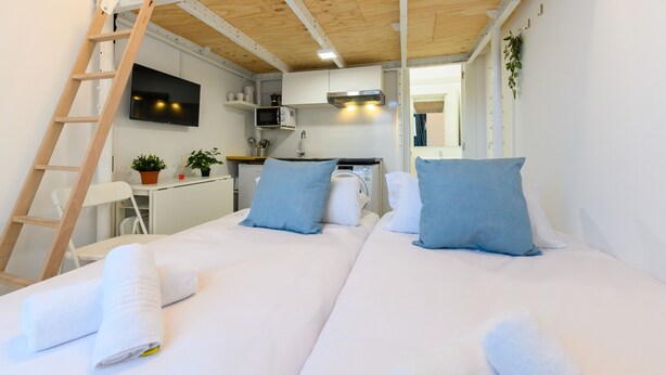Quarto de hotel com duas camas, televisão, micro-ondas, pia e pequena cozinha.