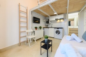 A compact room with a bed, a small table with a plant, a chair, a washing machine, a microwave, and a TV. - M Rbl180 Acogedor d Plex en Salamanca (Madrid)