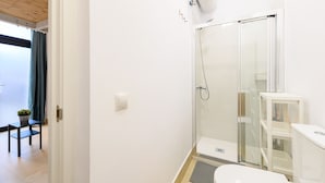 Um banheiro moderno com box de vidro, vaso sanitário e uma pequena mesa com uma planta.