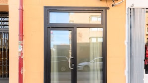 Um edifício com porta de vidro emoldurada por preto, um poste vermelho com adesivos e um portão de metal.