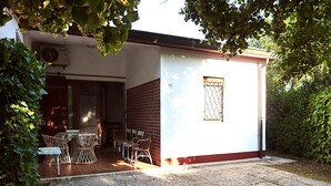 Ein kleines Gebäude mit einer Terrasse, einem Tisch mit Stühlen und einem Fenster mit einem Metallgitter.