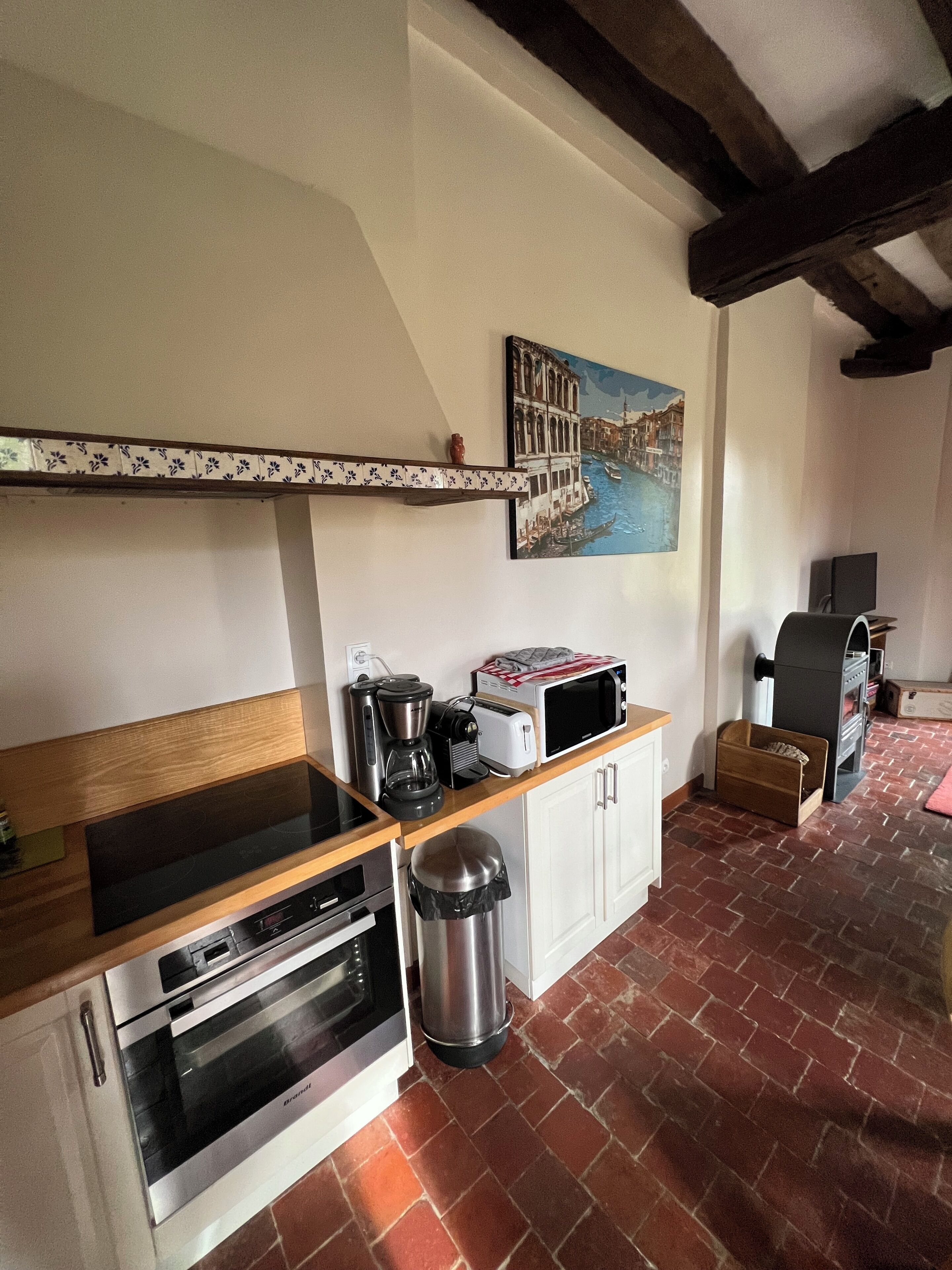 A compact kitchen with a built-in oven, a coffee maker, a microwave, and a small trash bin.