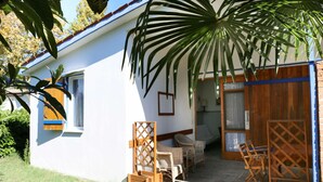 Et lille, etages hus med hvide vægge og et blåt tag. Der er en terrasse med fletmøbler og et træbord.