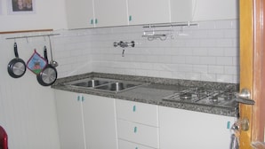 Et køkken med hvide skabe, en granitbordplade, en dobbeltvask og en gasblus.