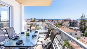 Ein Balkon mit Glastisch, gedeckt für ein Essen, mit Blick auf eine Skyline aus Gebäuden und einem klaren Himmel.