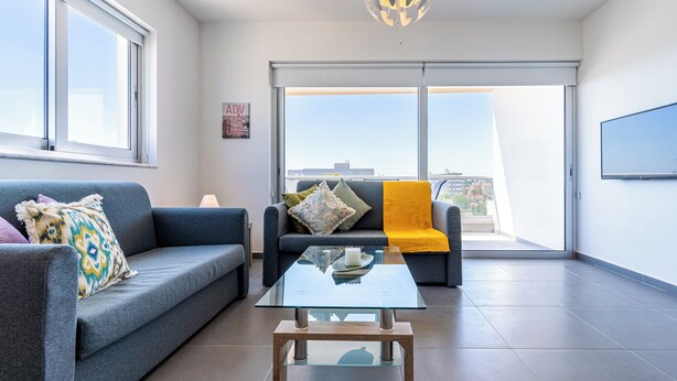 Ein modernes Wohnzimmer mit einer Couch, einem Glastisch und Blick durch eine Glastür auf einen Balkon.