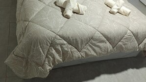 Una cama con un edredón color beige, dos toallas enrolladas y una mesita de noche negra.