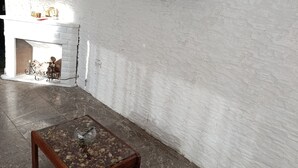Una habitación con pared de ladrillo blanco, televisor montado, mesa de centro de madera y chimenea con una bicicleta y elementos decorativos.
