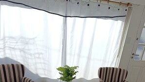 Una habitación con dos sillones a rayas, una mesita con una planta en maceta y una ventana con cortinas.
