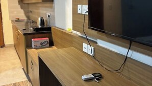 Eine moderne Küche mit Flachbildfernseher an der Wand, einer Arbeitsplatte mit Wasserkocher, Taschentuchbox und Fernbedienung.