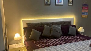 Un lit bien fait, avec une couvre-lit à motifs, une lampe de chevet et une table de chevet dotée de tiroirs.