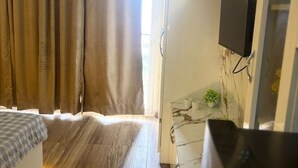 Une chambre d’hôtel avec un lit, des rideaux, un téléviseur fixé au mur et une petite plante sur la table de chevet.